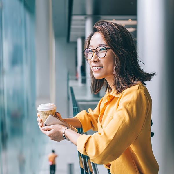 Smilende kvinde, der holder en kaffekop og kigger udenfor