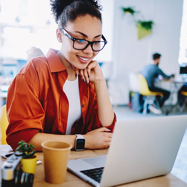 Smilende kvinde, der ser på sin bærbare computer i en kaffebar