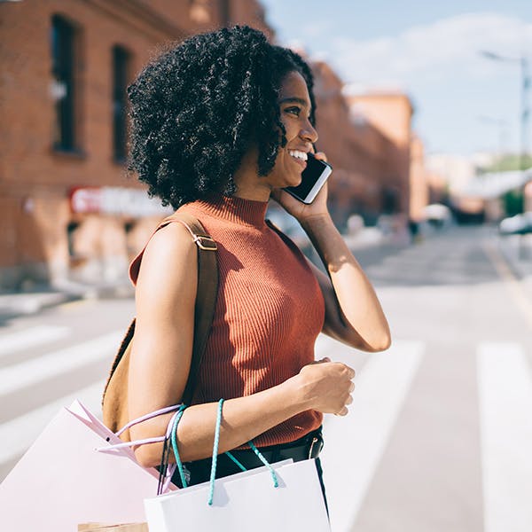 Kvinde, der går på tværs af gaden på telefonen med indkøbsposer
