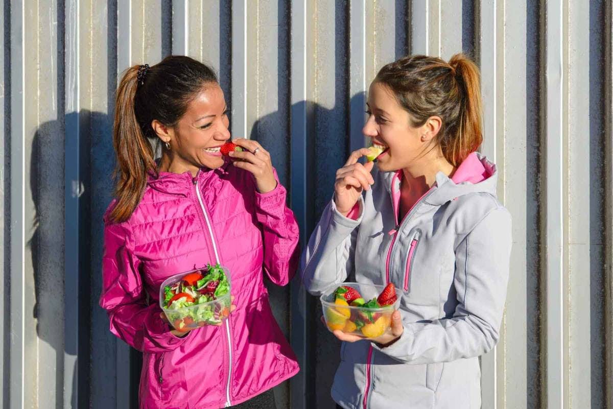 Two women laughing while eating salad in workout gear