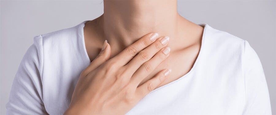 woman in white touching her chest with grey background