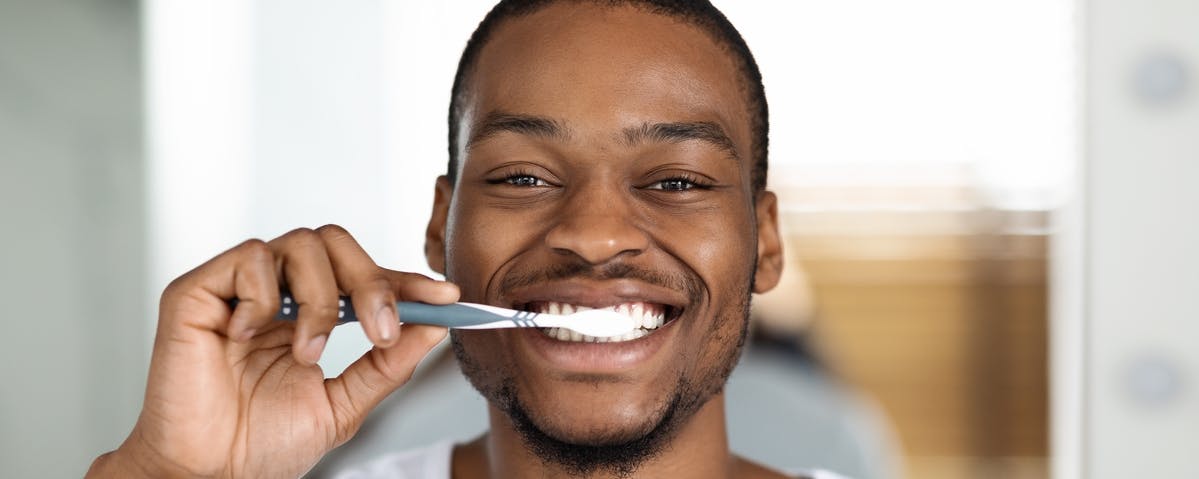 Man in white tee smiling while brushing his teeth