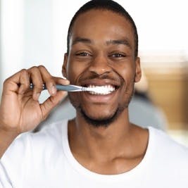 Man in white tee smiling while brushing his teeth