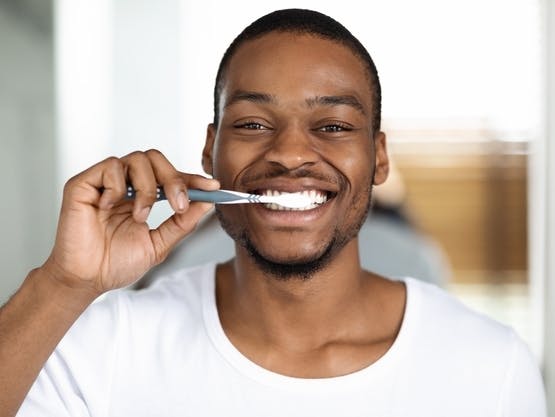 Man in white tee smiling while brushing his teeth