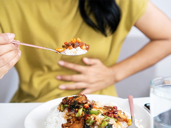 Woman eating spicy food holds her abdomen while experiencing heartburn Woman eating spicy food holds her abdomen while experiencing heartburn