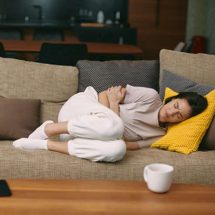 Women holding chest on couch with coffee cup on counter