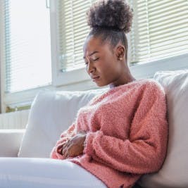 Woman on couch holding stomach with pained expression