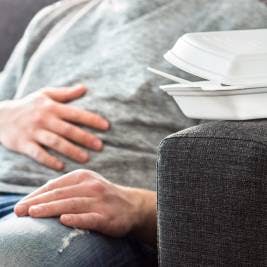 Man on couch with acid reflux after eating takeout food