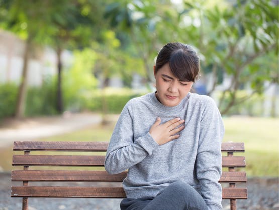 Mujer sentada en una banca del parque experimentando acidez estomacal frecuente
