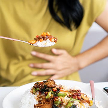 Mujer comiendo con la mano presionada contra el estómago