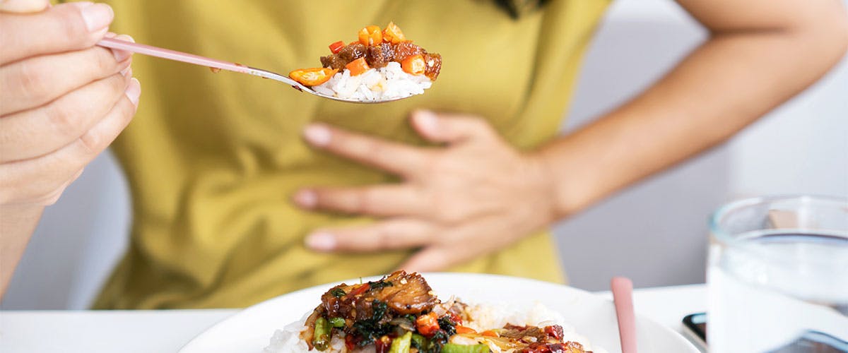 Woman eating food with hand pressed against stomach