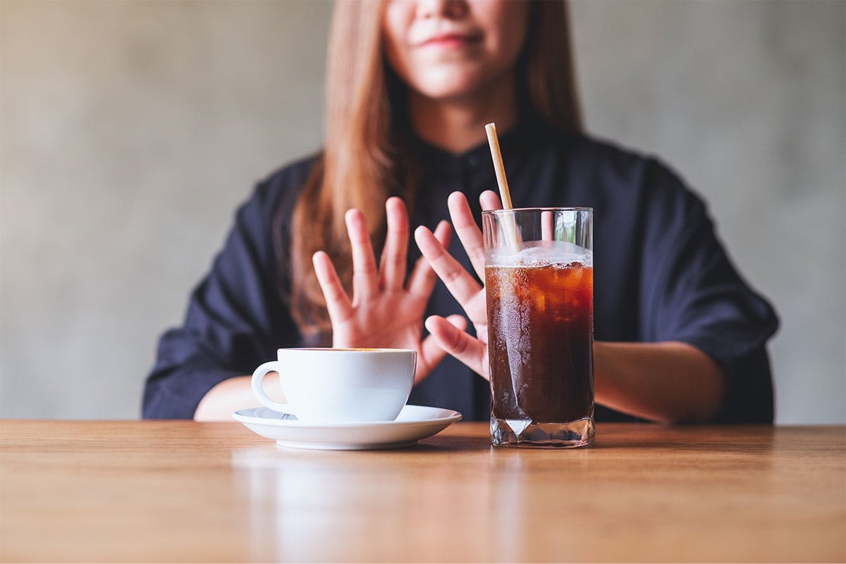 Mujer joven rechaza una taza de café y un refresco con cafeína. Mujer joven rechaza una taza de café y un refresco con cafeína.