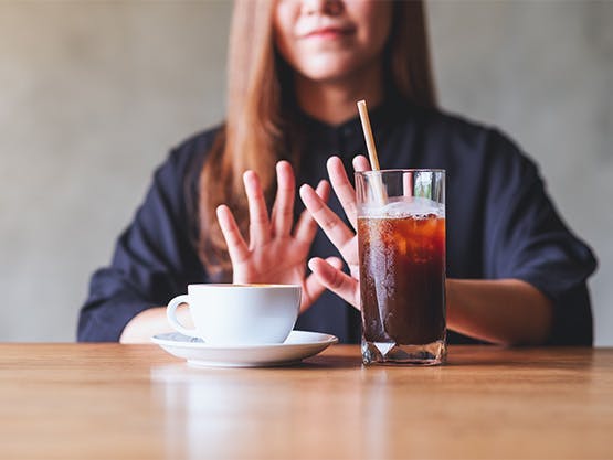 Mujer joven rechaza una taza de café y un refresco con cafeína.