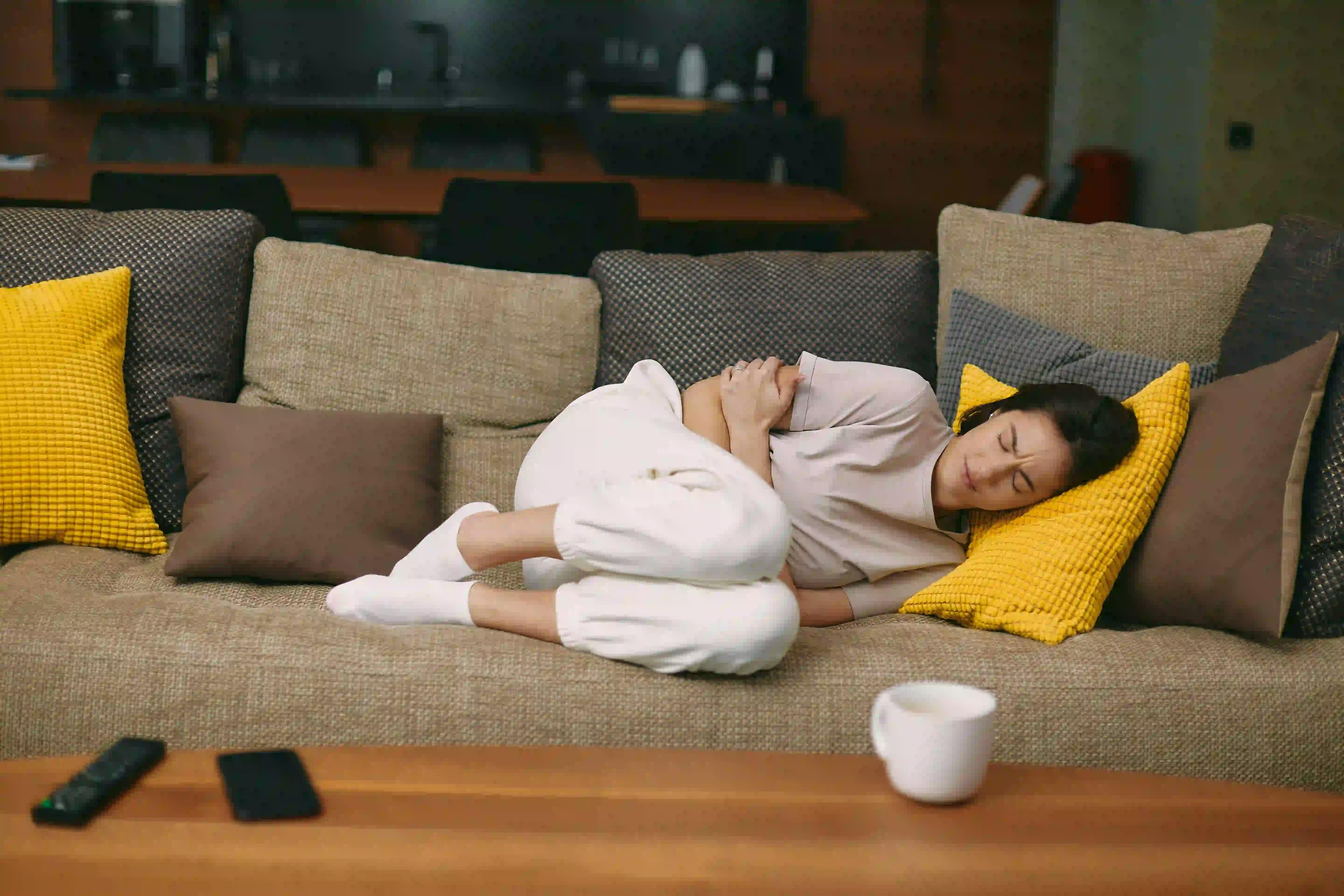 Women holding chest on couch with coffee cup on counter