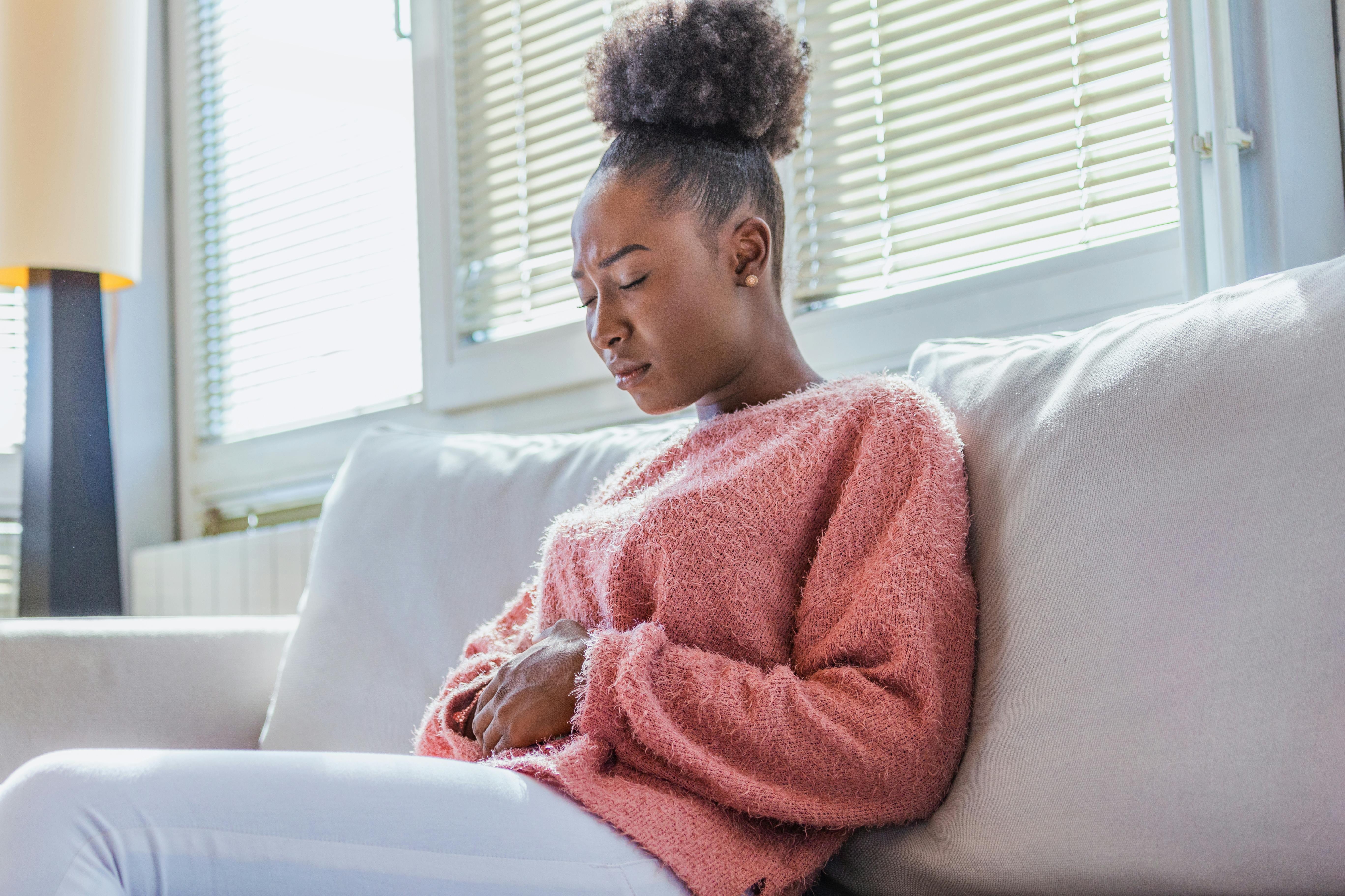 Woman on couch holding stomach with pained expression Woman on couch holding stomach with pained expression