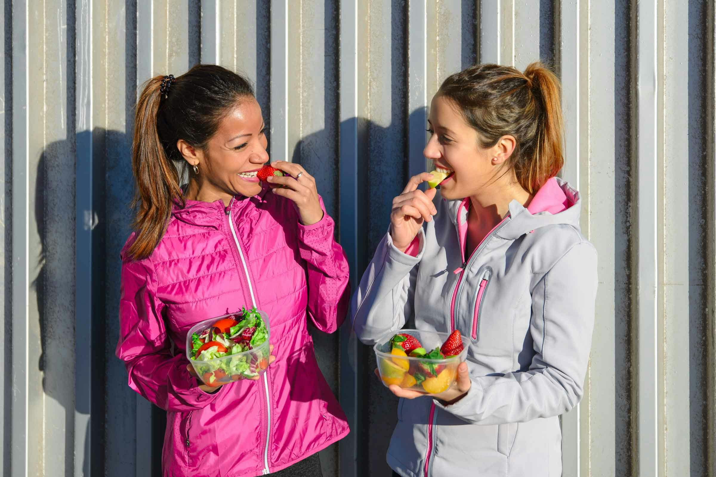 Two women laughing while eating salad in workout gear