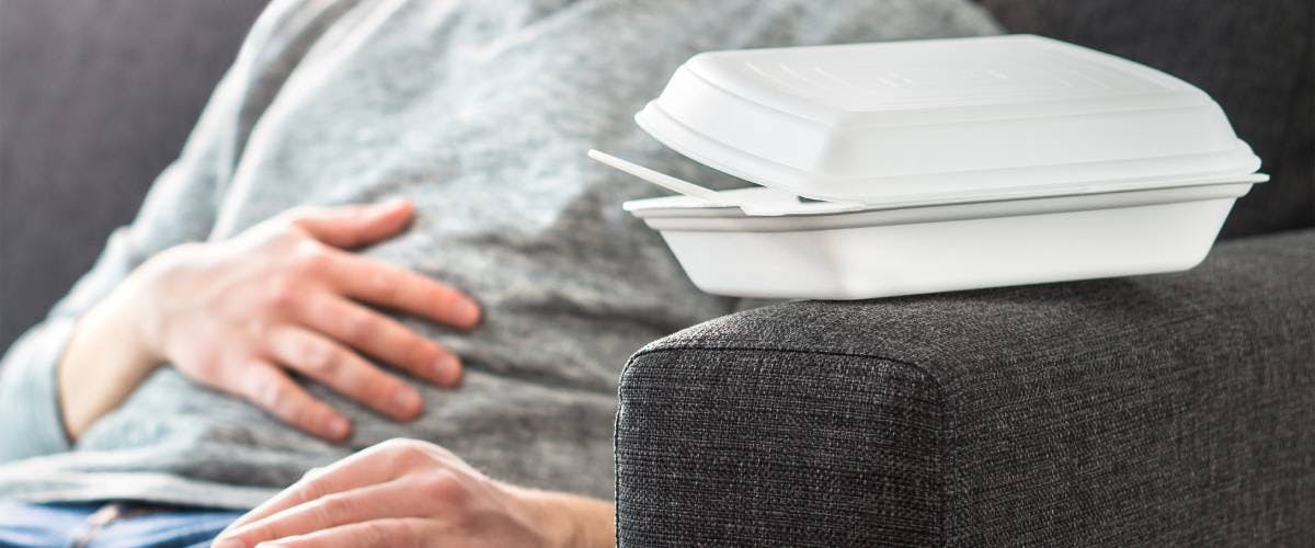 Man on couch with acid reflux after eating takeout food