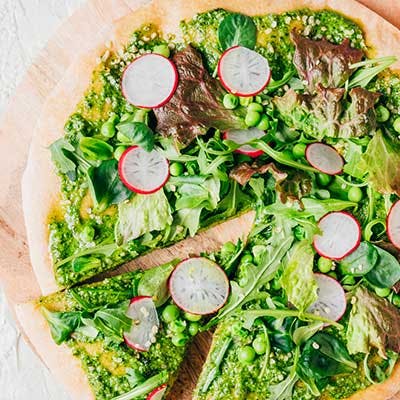 Pizza with green pesto, arugula, peas and radish