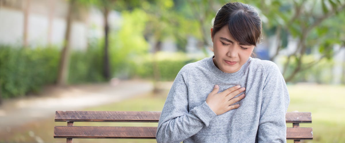 Woman sitting on park bench experiencing frequent heartburn