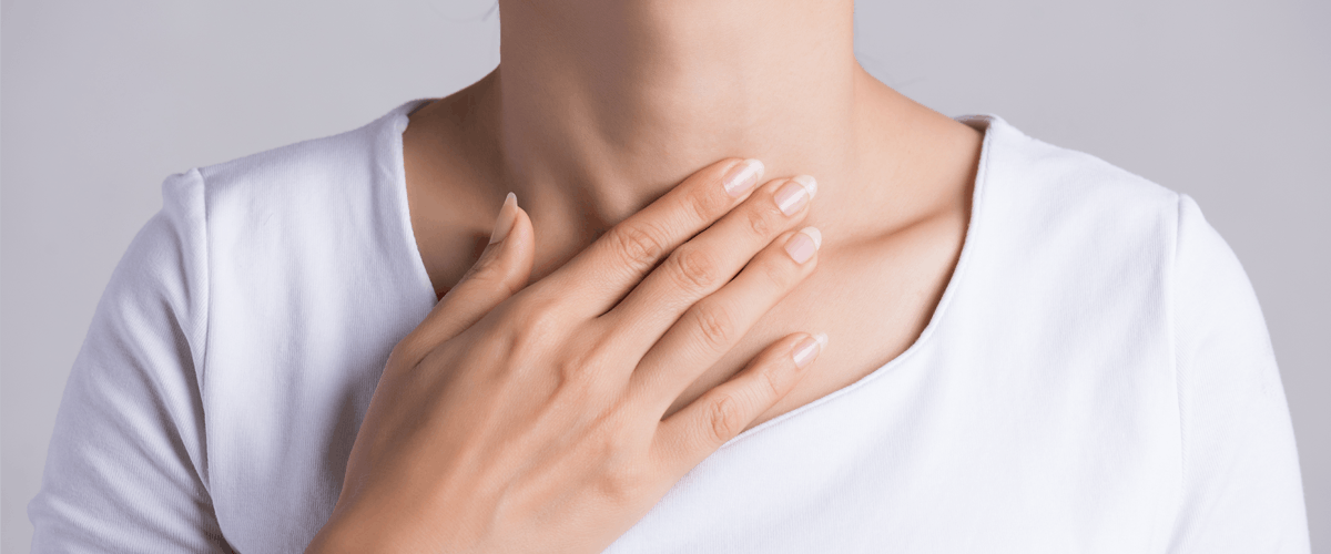 woman in white touching her chest with grey background 