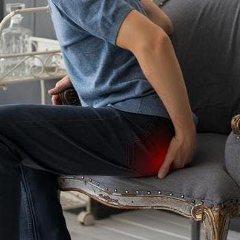 man in blue jeans sitting on gray chair rubbing buttocks in pain