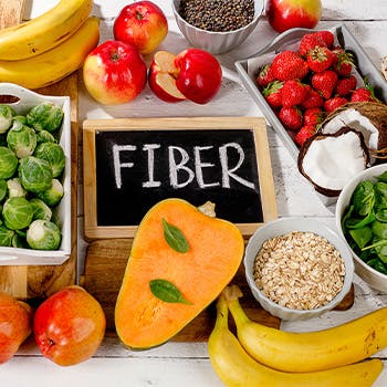 High fiber foods: brussels sprouts, apples, oats, spinach, and more arranged around a chalkboard that reads “Fiber”