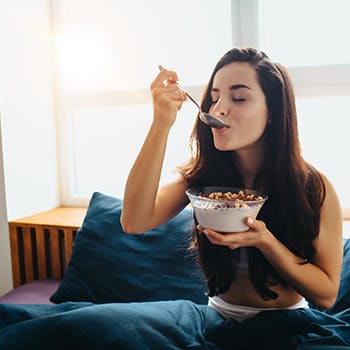 Young woman eating whole grains in bed