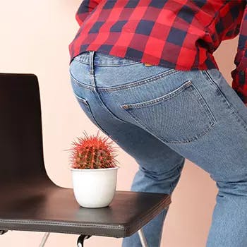 Man about to sit on a chair with a cactus plant on it, symbolizing hemorrhoids pain