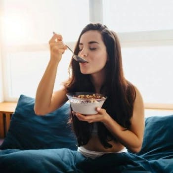 Young woman eating whole grains in bed