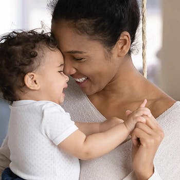 Woman sitting on the floor lifts her baby in the air