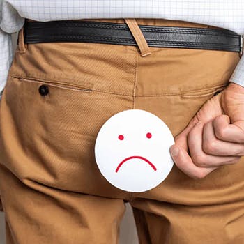 A man holds a drawing of a frowning face over his posterior to indicate that he has hemorrhoids