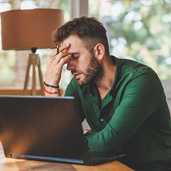 Man holding forehead over laptop