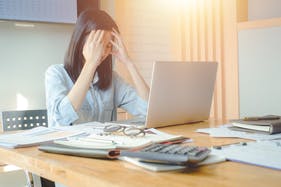 Stressed woman sitting at desk in front of laptop with head in her hands Stressed woman sitting at desk in front of laptop with head in her hands