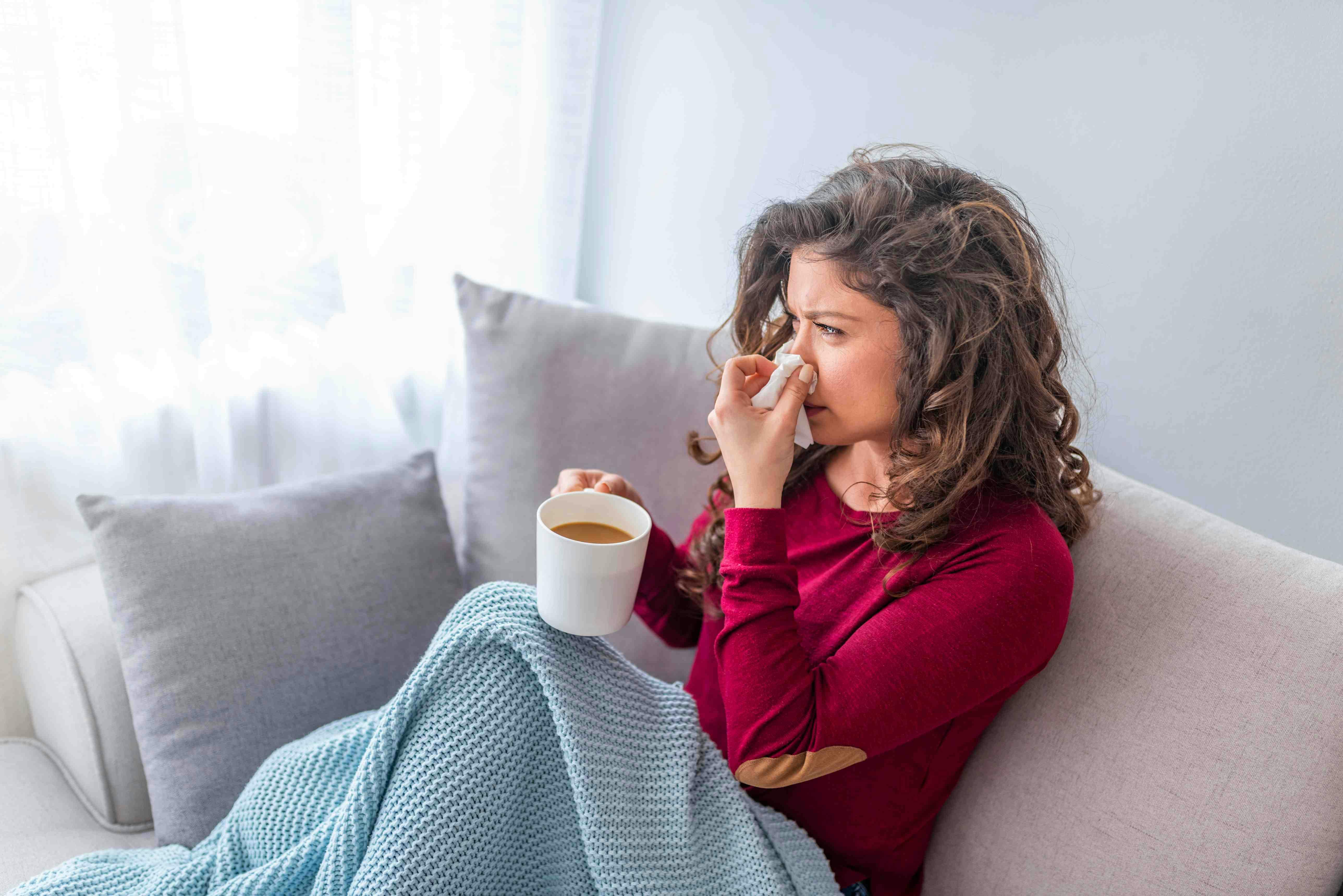 Woman blowing nose on couch 