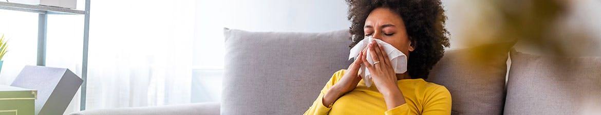 Woman suffering from allergies sneezes into a tissue