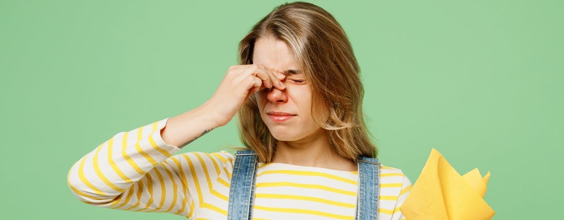 A women in a overalls and yellow striped shirt experiencing allergies