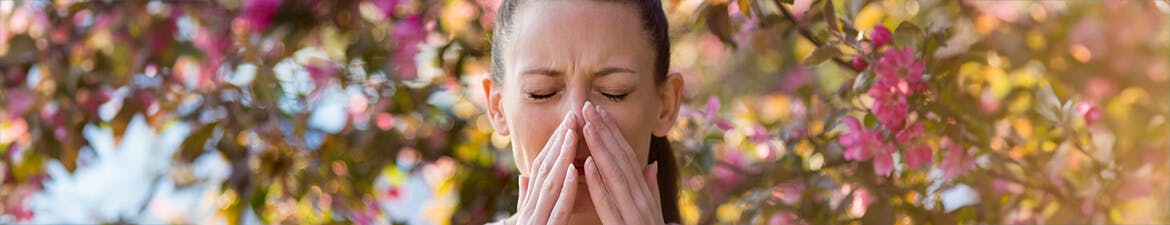 Woman sneezing in front of blooming tree
