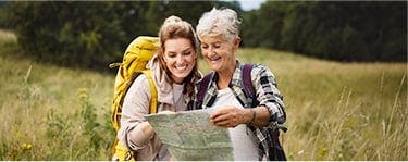 Young woman and older woman look at a map while hiking