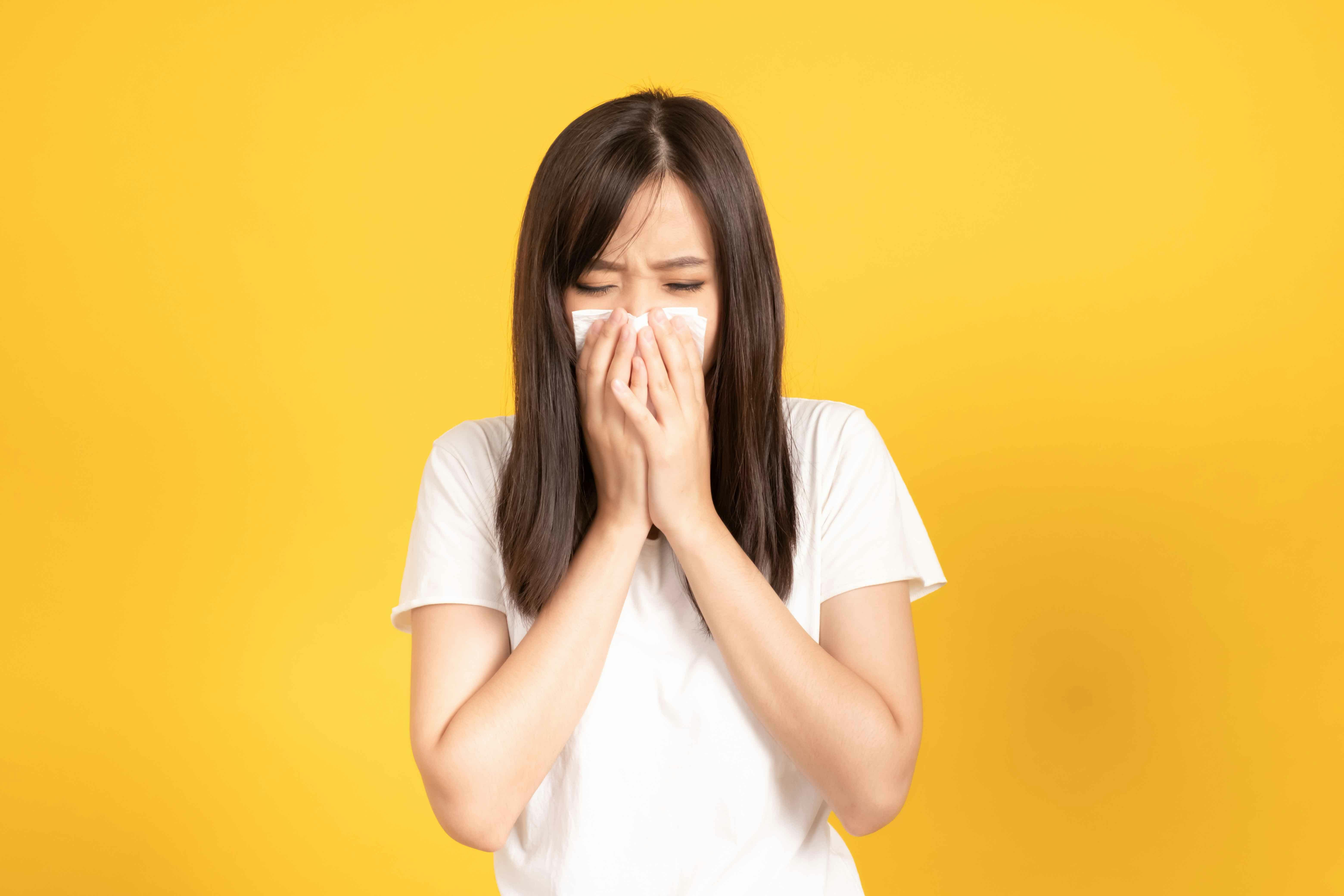 A woman sneezing with tissue in her hands