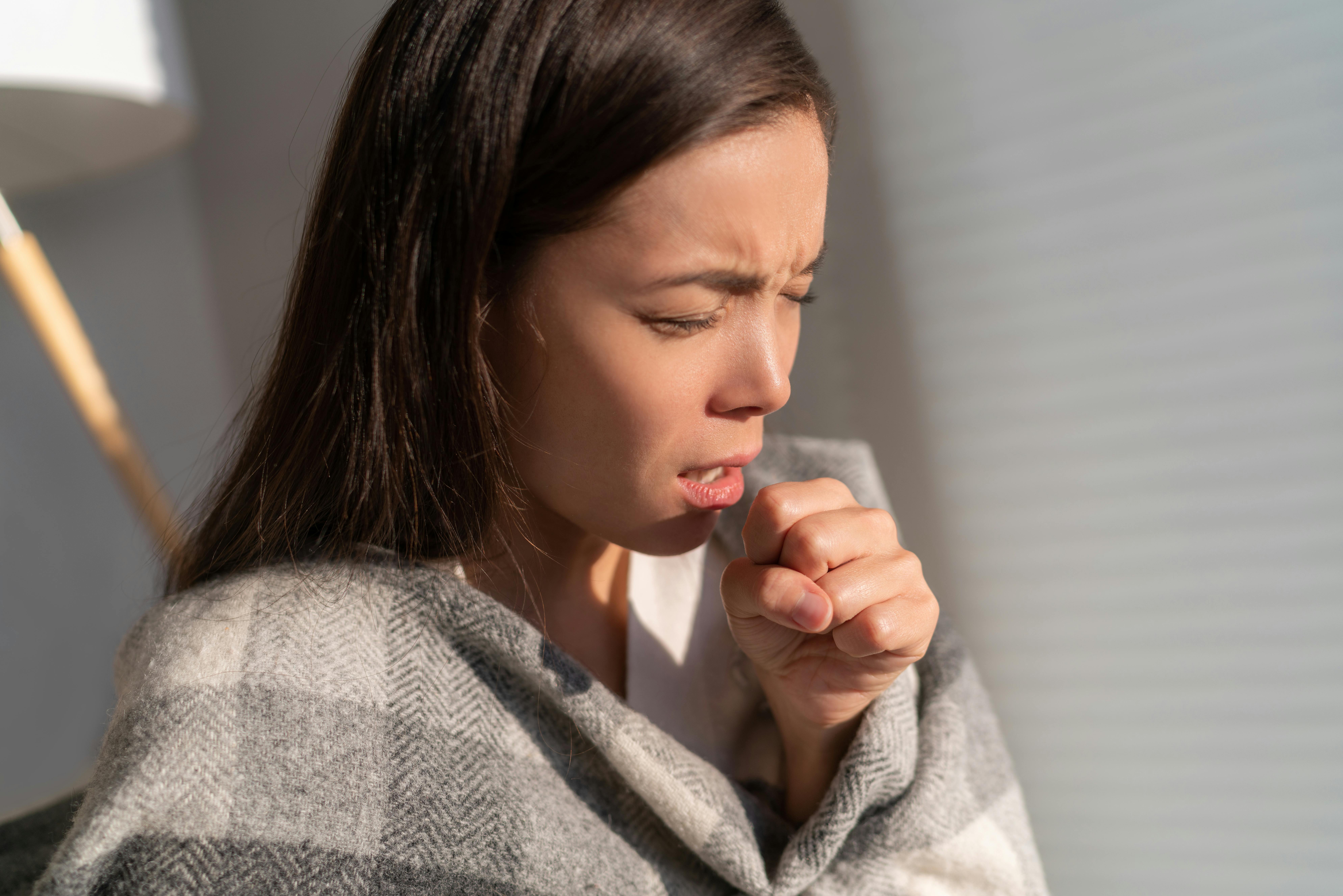 Young woman coughs into her hand with a blanket around her shoulders