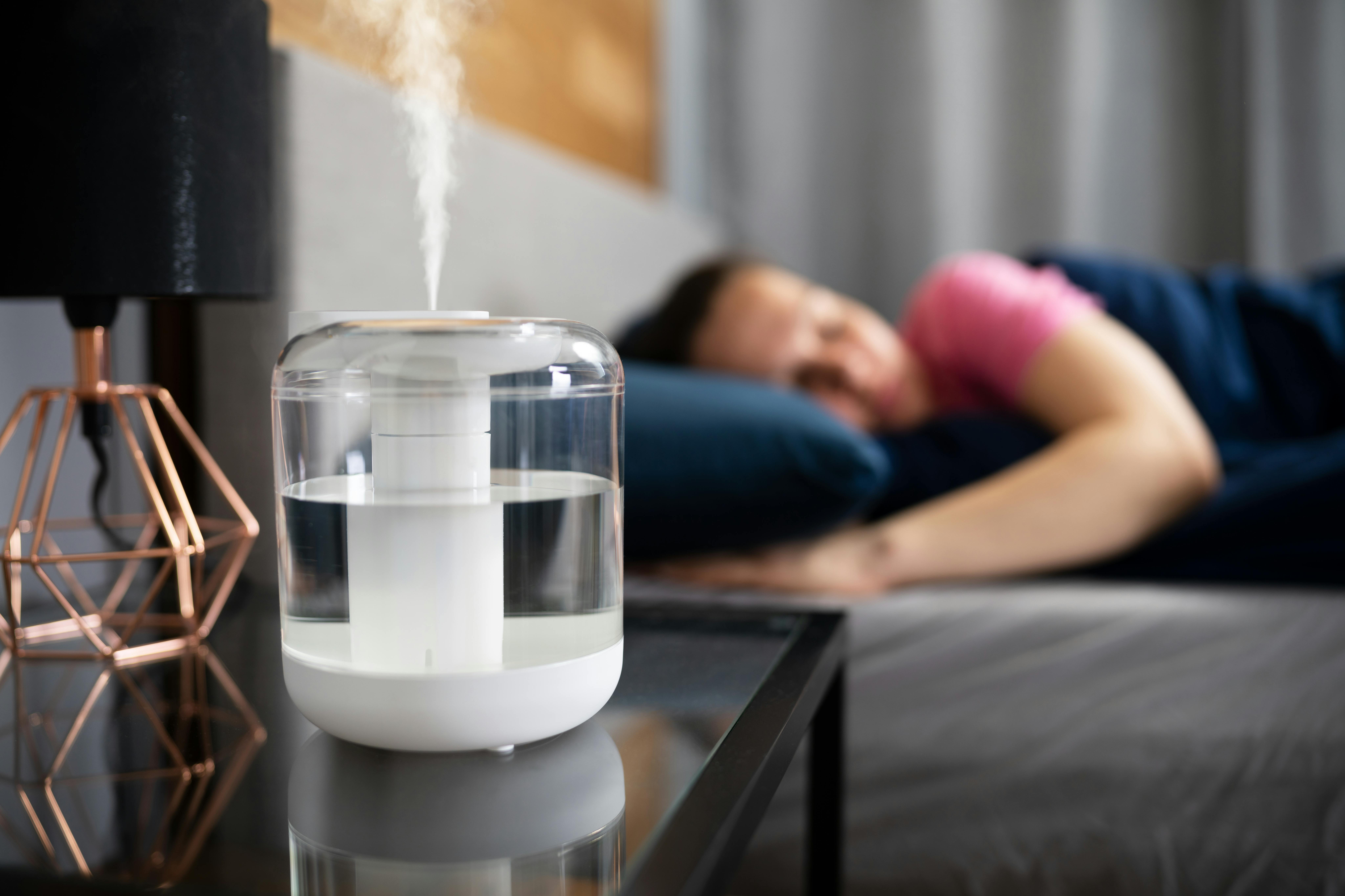 A young woman sleeps in bed with a humidifier running nearby.