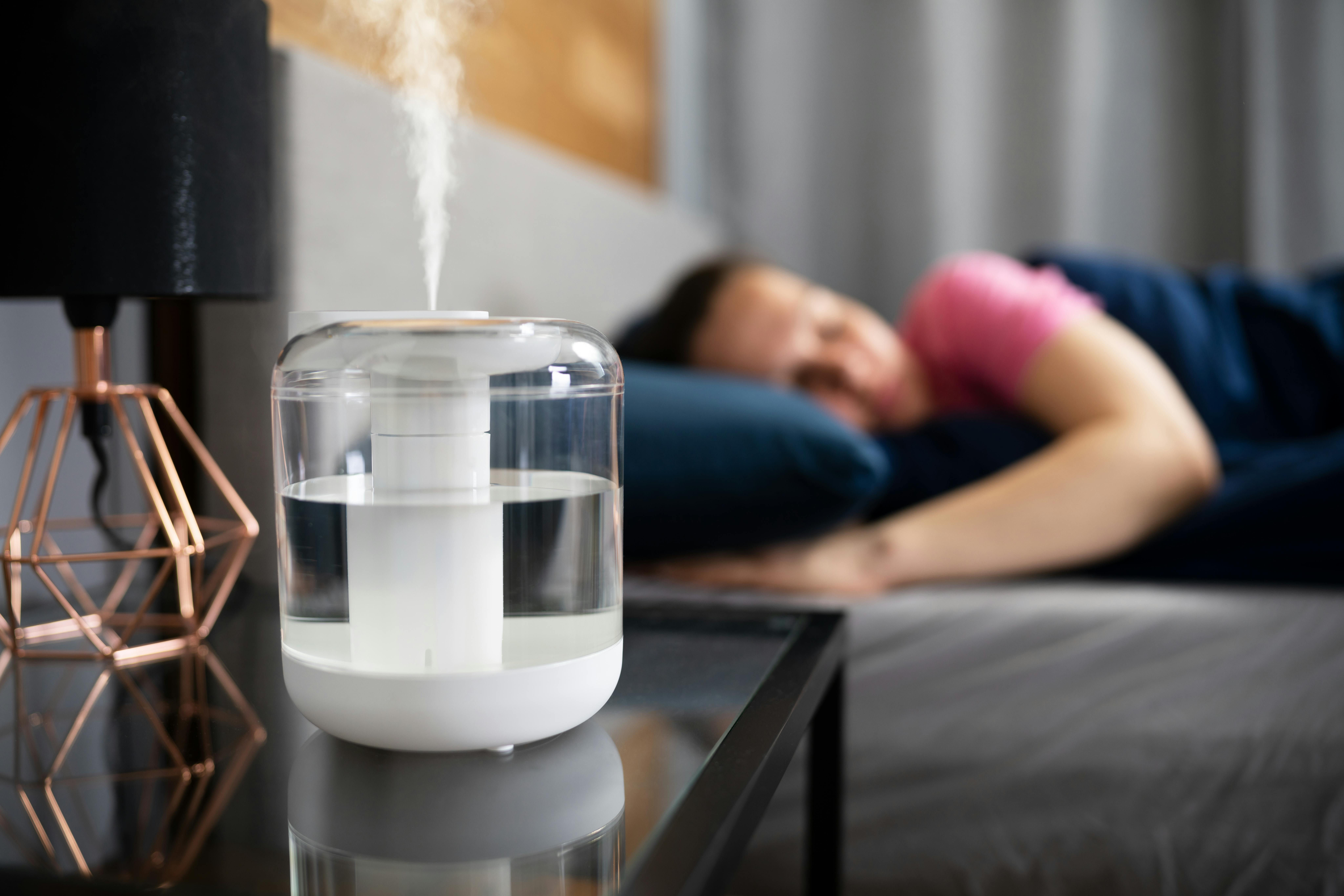 A young woman sleeps in bed with a humidifier running nearby. A young woman sleeps in bed with a humidifier running nearby.