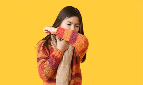 Kid in cozy sweater coughing into her sleeve