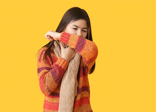 Kid in cozy sweater coughing into her sleeve