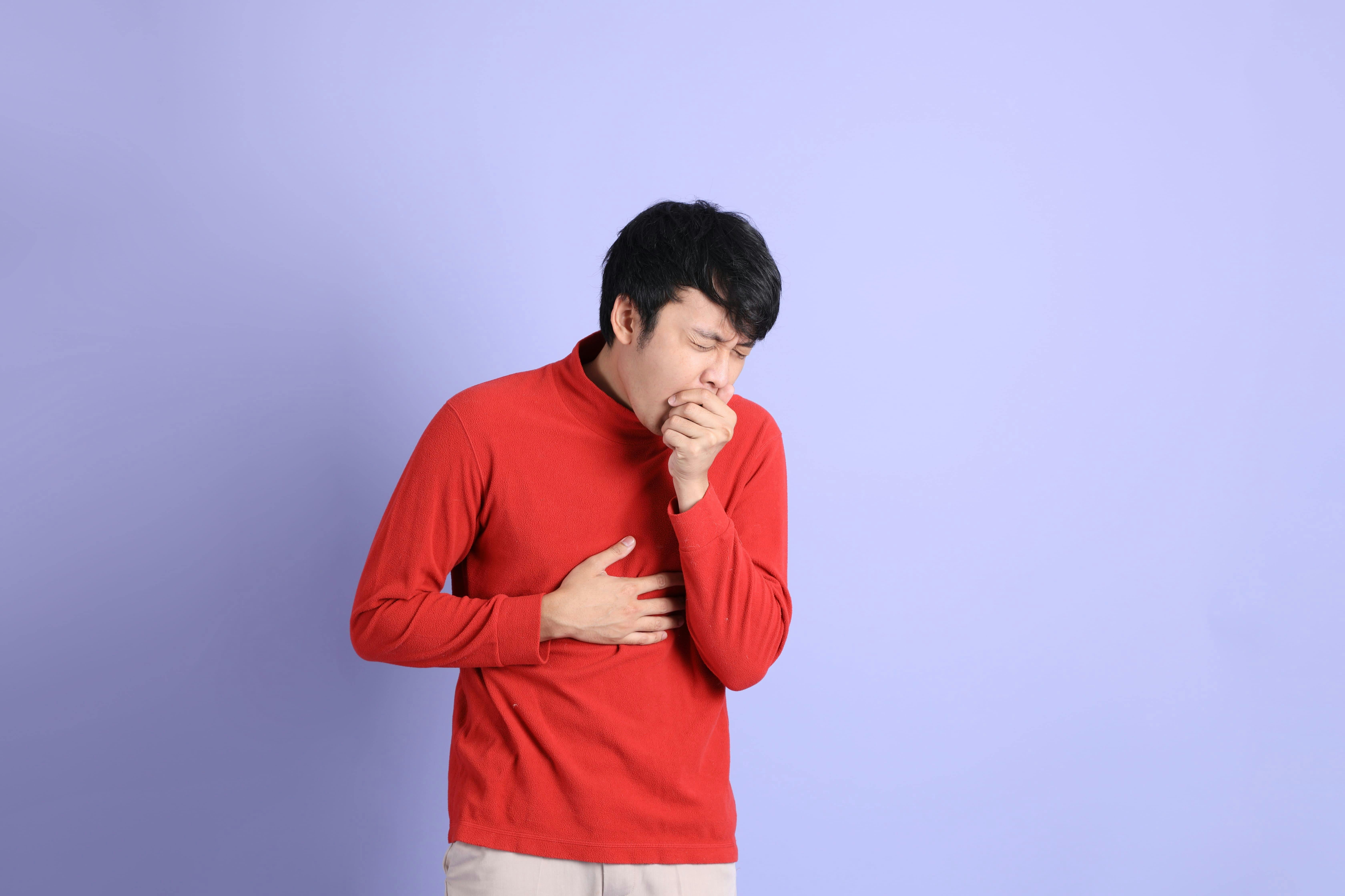 Asian man in red shirt coughs into his hand