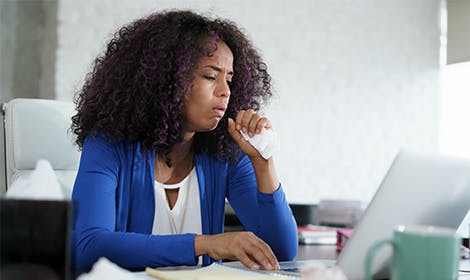 Woman coughing into fist while working