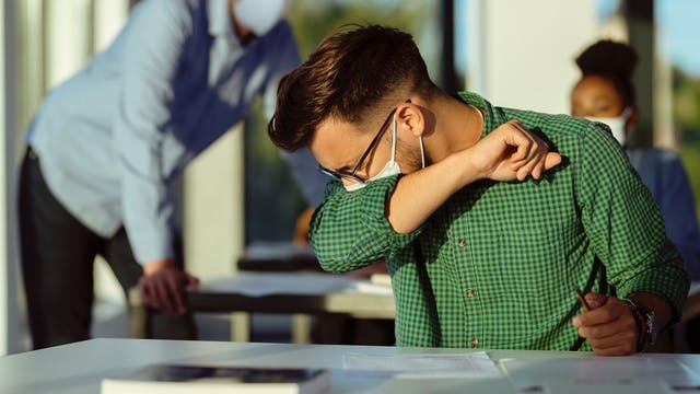 Man coughing into arm while wearing face mask