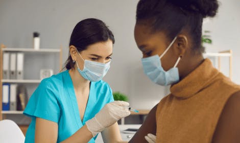 Medical professional in a face mask giving a vaccine to a patient