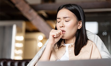 Woman coughing in front of laptop