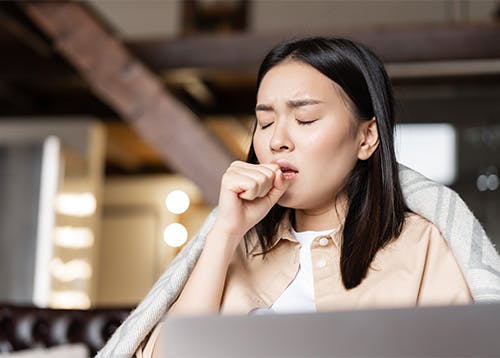 Woman coughing in front of laptop